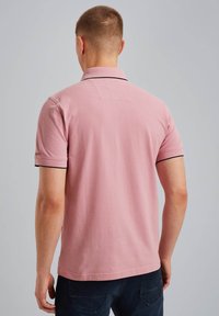 Chemise polo rose à manches courtes, avec un col noir et un ourlet droit. Présente une texture lisse et des détails de couture subtils sur les manches.