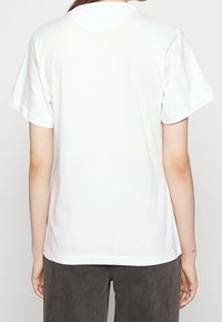 Bílé bavlněné tričko s krátkými rukávy a kulatým výstřihem. Jednoduchý design, žádné vzory ani ozdoby, hladká textura.