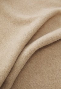 Lys beige uldstof, blød tekstur, med subtile farvevariationer. Glatte, foldede lag viser et hyggeligt udseende.