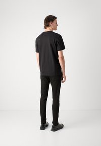 T-shirt in cotone nero con maniche corte, vestibilità regolare. Indossato con pantaloni neri e scarpe nere. Design minimale, texture liscia, senza motivi.