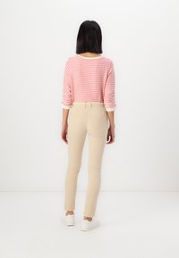Pantaloni beige aderenti e una maglietta a righe rossa e bianca a maniche lunghe. L'outfit presenta un design rilassato con maniche arrotolate e dettagli in tessuto morbido.