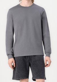 Graues Langarm-T-Shirt aus Baumwolle mit rundem Ausschnitt und geradem Saum, kombiniert mit dunkelgrauen Shorts mit Kordelzug und weicher Textur.