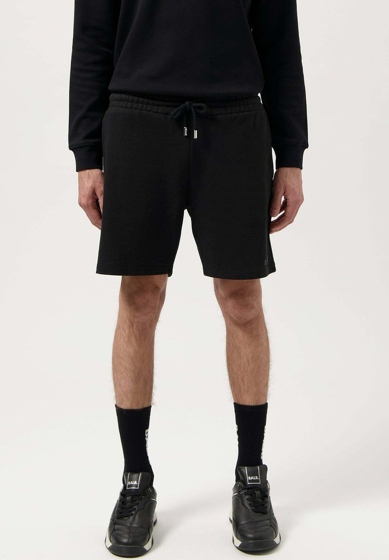 Black cotton shorts with an elastic waistband and drawstring, featuring a relaxed fit and above-knee length. Worn with black socks and sneakers.