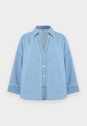 Gaiši zilas džinsa jakas ar platām piedurknēm, noapaļotu apkakli un priekšpusē sudraba spiedpogas uz vienkārša balta fona.