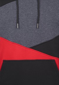 Mikina s kapucí v designu barevných bloků se šedými, červenými a černými částmi, vyrobená z měkké látky s přední kapsou ve tvaru klokaní kapsy.