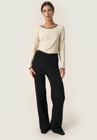 Maglietta beige a maniche lunghe con rifiniture nere, abbinata a pantaloni larghi a coste neri. Tessuto morbido e motivi testurizzati in tutto il capo.