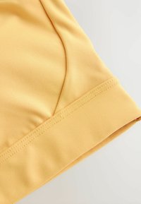 Sárga anyagból készült ruhadarab, sima textúrával, ívelt nyakkivágással és gondosan varrott szegéllyel. A dizájn egyszerű és letisztult.