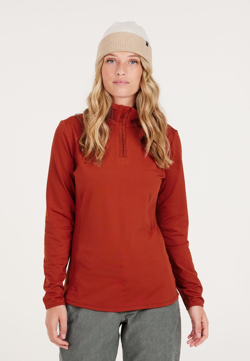 Roodbruine langemouwen top met hoge kraag, ritsdetails en aansluitende mouwen, gecombineerd met een beige gebreide beanie. Getextureerde stof.