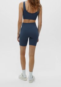 Šedá sportovní podprsenka a cyklistické kraťasy vyrobené z elastického materiálu, s bezešvým designem a vysokým pasem pro podporu a pohodlí.
