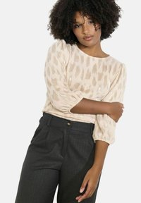 Světle béžový top s texturovaným, abstraktním vzorem; tříčtvrteční balónové rukávy; v kombinaci s tmavě šedými kalhotami na míru s knoflíkovým zapínáním.