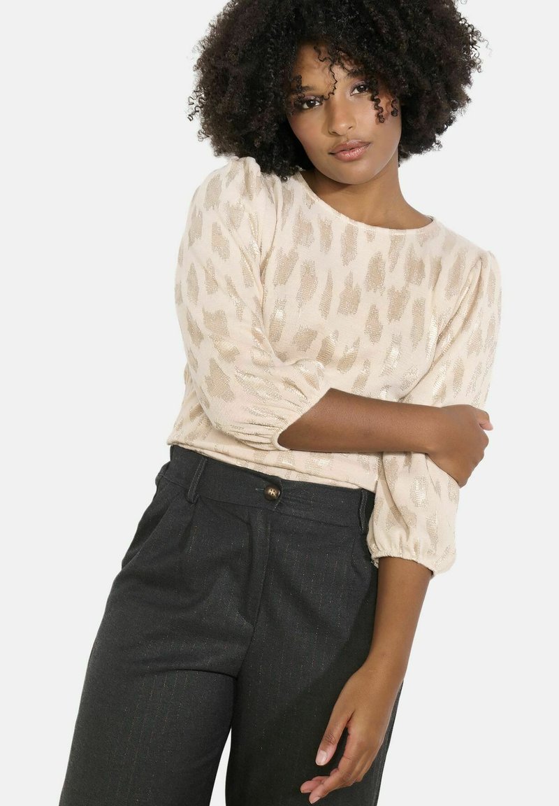 Světle béžový top s texturovaným, abstraktním vzorem; tříčtvrteční balónové rukávy; v kombinaci s tmavě šedými kalhotami na míru s knoflíkovým zapínáním.