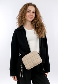 Borsa a tracolla beige trapuntata dalla forma rettangolare, con superficie testurizzata e tracolla removibile. Decorata con una cerniera nera e accessori.