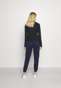 Schwarzes langärmliges Oberteil und marineblaue Jogginghose mit lockerem Schnitt und gerippten Bündchen, kombiniert mit weißen Sneakers vor neutralem Hintergrund.