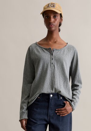 Grijze langhandige henleyshirt met een ronde halslijn en een knoopsluiting met drie knopen, gecombineerd met donkerblauwe hooggeritste jeans.