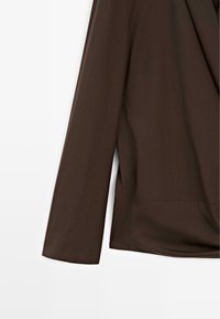 Rechter mouw en zijkant van een donkerbruin colbert met lange mouwen op een witte achtergrond.