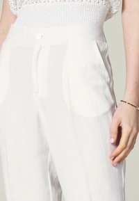 Bílé lněné kalhoty s vysokým pasem, s předním zapínáním na knoflík, bočními kapsami a jemnou, texturovanou tkaninou.
