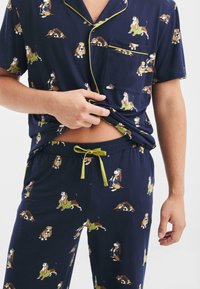 Conjunto de pijama en color marino con perros de dibujos animados en varias posturas. Camisa de manga corta con bolsillo, pantalones con cintura elástica y cordón. Accentos brillantes.