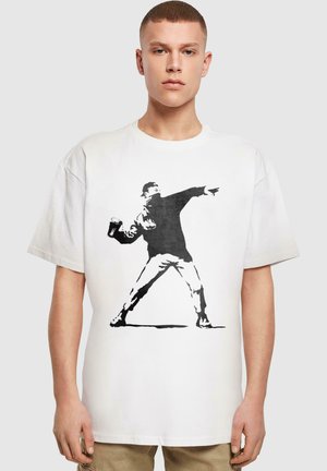 White cotton oversized t-shirt featuring a black graphic of a person throwing a can, with a distinct silhouette design.