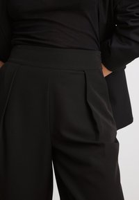 Zwarte hooggetailleerde broeken met geplooide voorkant. Gemaakt van gestructureerde stof, met een op maat gemaakte uitstraling en een gladde afwerking.