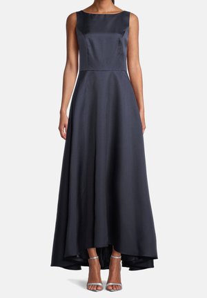 Granatowa wieczorowa sukienka z satyny bez rękawów, z dekoltem w łódkę i asymetrycznym dołem, noszona z srebrnymi szpilkami z paskiem wokół kostki.