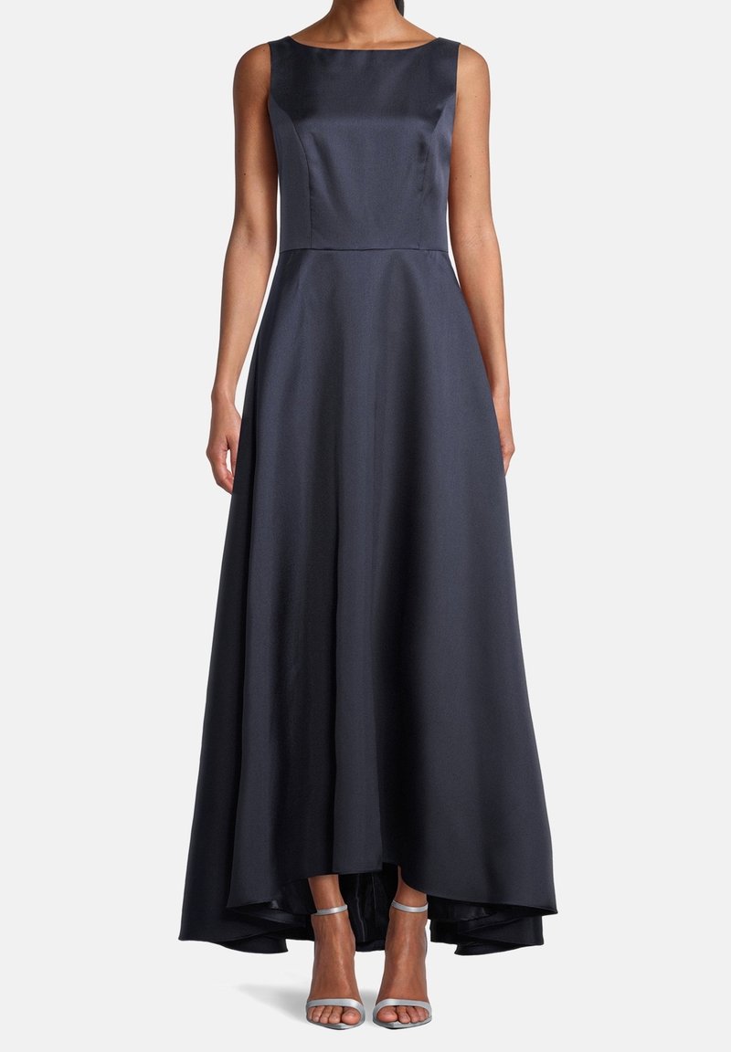 Robe de soirée en satin bleu marine sans manches, avec encolure bateau et ourlet asymétrique, portée avec des talons argentés à bride cheville.