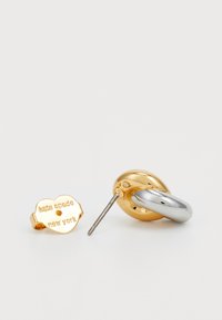 Guld- och silverörhängen med en hjärtformad plugg med engraven "kate spade new york" och en böjd, metallisk ring.