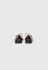 Zapatos de charol burdeos con un diseño elegante y tiras delgadas en marrón; tacones bajos en negro. La vista trasera resalta la textura suave y brillante.