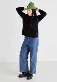 Black sweatshirt with white stitching, paired with wide-leg blue jeans. The model wears a green beanie and black platform shoes.