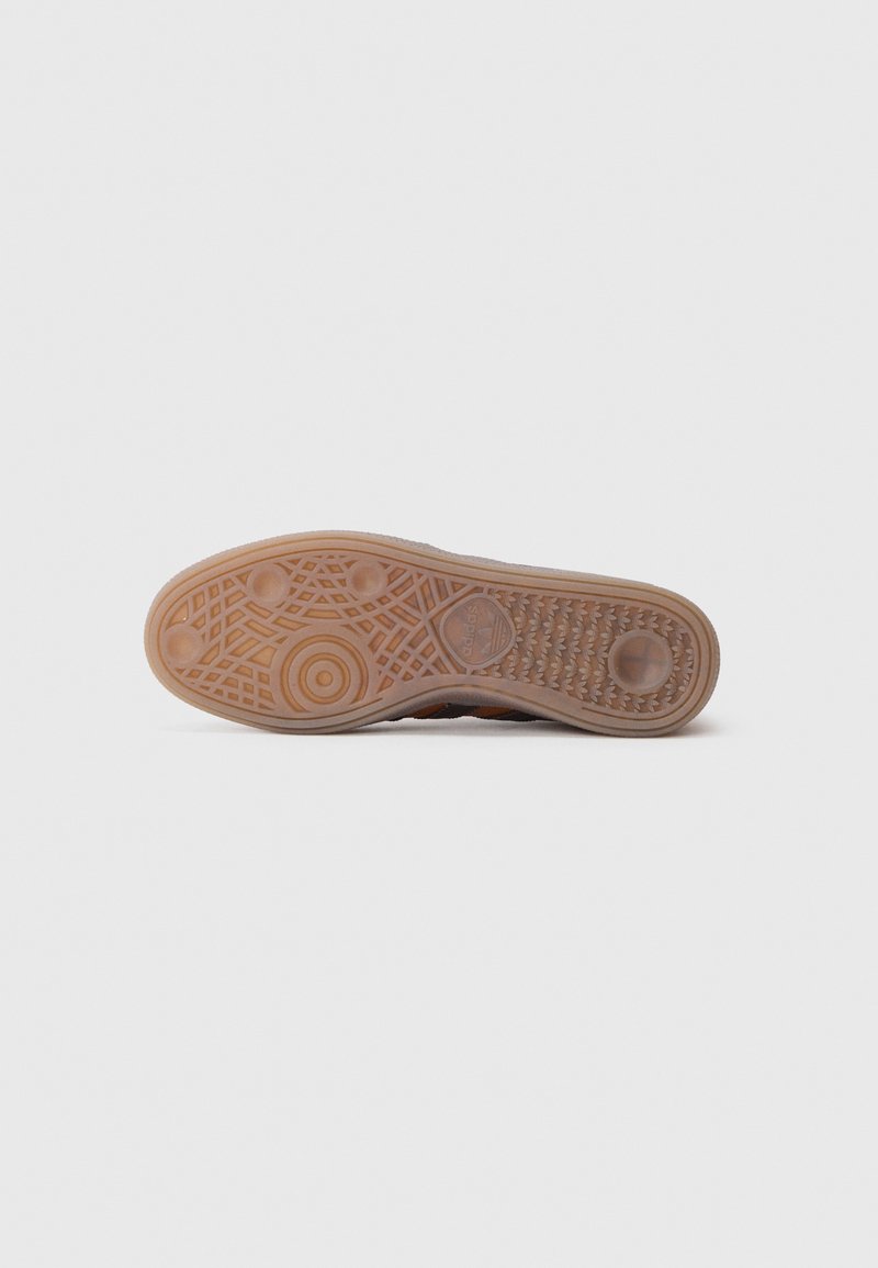 Shoe outsole with a textured rubber surface, featuring a circular pattern, raised sections for grip, and a beige color.