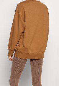 Sudadera marrón de gran tamaño hecha de una tela suave, con puños y dobladillo acanalados, combinada con leggings a rayas de color marrón claro.