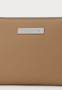 Brązowy skórzany portfel o gładkiej fakturze, z metalową płytką w kolorze srebrnym z nazwą marki. Kompaktowy prostokątny kształt.