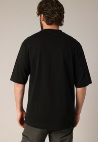 T-shirt noir à manches courtes en coton, avec un col rond et une coupe décontractée. L'ourlet cousu et le design sans étiquette améliorent le confort.