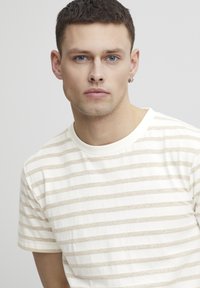 Stripete T-skjorte i krem og beige, laget av bomull, kortermet, rund hals, har horisontale striper med en myk tekstur.