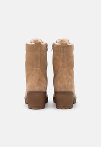Stivaletti alla caviglia in suede beige, con tacco arrotondato, chiusura con zip e morbida fodera in pelliccia sintetica. Presentano una texture liscia e una suola robusta e texturizzata.