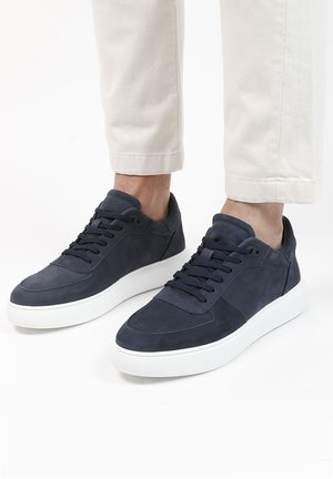 Navy suede sneakers with a white rubber sole, featuring perforated details, lace-up closure, and a padded collar for comfort.