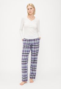 Haut henley à manches longues blanc avec trois boutons, associé à un pantalon de pyjama ample à carreaux dans des motifs violet, noir et blanc.