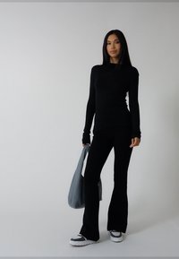 Fekete hosszú ujjú felső és bővülő szárú nadrág, szürke bevásárlótáskával párosítva. A cipők fehér-fekete mintásak, lekerekített orrú kialakítással.