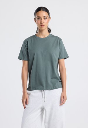 Dark green cotton t-shirt with short sleeves, crew neckline, relaxed fit, paired with gray sweatpants. Smooth texture, no visible patterns.