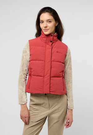 Rode puffer vest met hoge kraag, knopen aan de voorkant en zijzakken, gedragen over een lichtgekleurde lange mouw top en gecombineerd met beige broeken.
