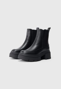 Bottines noires en cuir lisse, avec des panneaux latéraux élastiques, un talon épais et une semelle en caoutchouc texturé.
