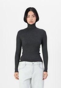 Mørk grå ribbestrikket genser med høy hals og lange ermer, med en figursydde design og teksturert stoff. Kombinert med lyse denimjeans.