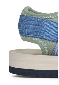 Πράσινο και μπλε υφασμάτινο σανδάλι με παχιά κρεμ μεσαία σόλα και σκούρα ναυτικού χρώματος εξωτερική σόλα. Τα αξεσουάρ περιλαμβάνουν λουράκια με σχέδια και ραμμένες λεπτομέρειες.