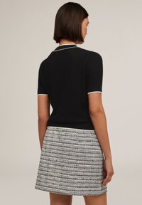 Pull noir à manches courtes avec tricot texturé, bordure blanche au niveau du col et des manches, associé à une jupe rayée noir et blanc.
