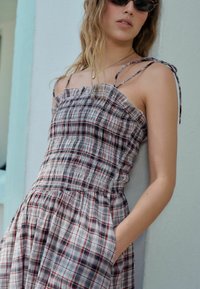 Un vestido de verano a cuadros con un cuerpo fruncido, escote con volantes y tirantes finos. Presenta una mezcla de patrones de cuadros en rojo, azul y blanco.