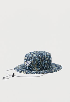 Námořnicky modrý klobouk s širokou krempou ve stylu bucket hat s béžovým tropickým potiskem a nastavitelným šňůrkovým páskem pod bradu s posuvníkem, položený na bílém pozadí.