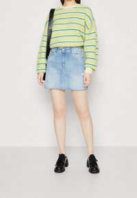 Pruhovaný žlutý a zelený svetr s dlouhými rukávy, doplněný světle modrou denimovou minisukní s třepeným lemem a roztrženým detailem. Černé boty.