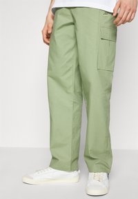 Lys grønne cargo bukser med en tekstureret finish, der har en sidelomme og en afslappet pasform, parret med hvide sneakers.