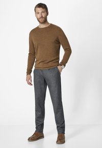 Brauner gestrickter Pullover, graue strukturierte Hose, braune Schnürschuhe und Armbanduhr; minimalistisches Design mit lockerer Passform.