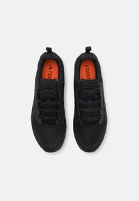 Czarne buty sportowe z siatkowym wierzchem, z czarnymi sznurowadłami, teksturowaną podeszwą i pomarańczową wkładką z logo marki.