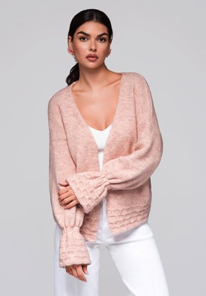 Rosa, mjuk stickad cardigan med V-ringning, vida ärmar med en strukturerad mönstring och öppen fram, kombinerad med en vit topp.